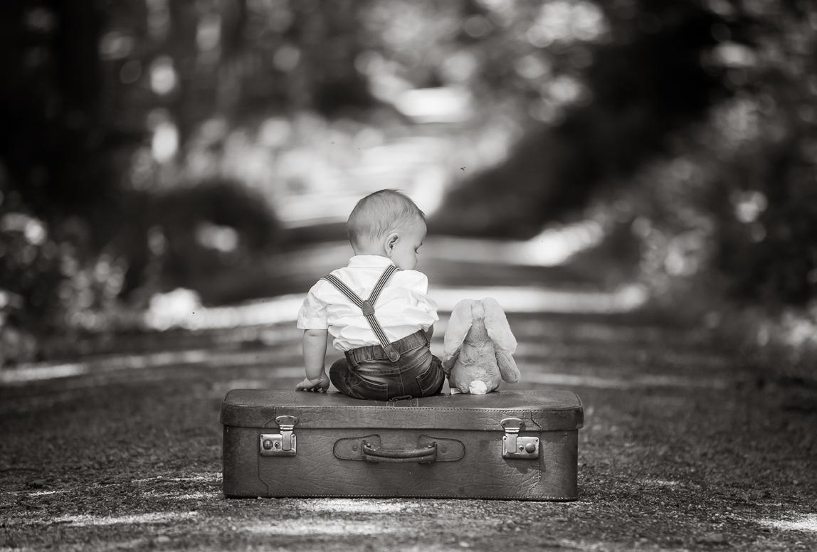 mallorca toddlers portrait photography - a baby sitting on a luggage with his stuffed bunny